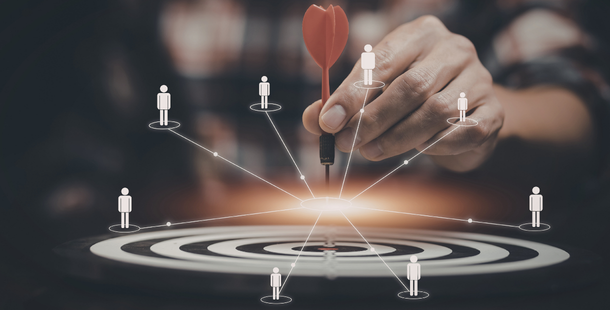 Man in plaid shirt holding a dart over the center of a target with lines coming from the center leading to graph representations of people.